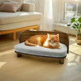 Charger l'image dans la visionneuse de la galerie, Lit canapé en bois pour chat avec coussin gris où un chat roux est couché dans un salon lumineux