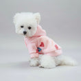 Charger l'image dans la visionneuse de la galerie, Chien blanc portant un sweat doux capuche chien rose avec motifs cœurs rouges assis sur une ottomane