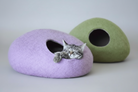 Chat endormi dans un cocon laine mérinos pour chat violet avec un autre vert en arrière-plan