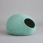 Cocon laine mérinos pour chat de couleur vert pastel posé sur une chaise en bois avec un plaid beige