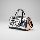 Grand sac de voyage pour chat et chien argenté avec poignées noires posé sur le sable à côté d'un chat