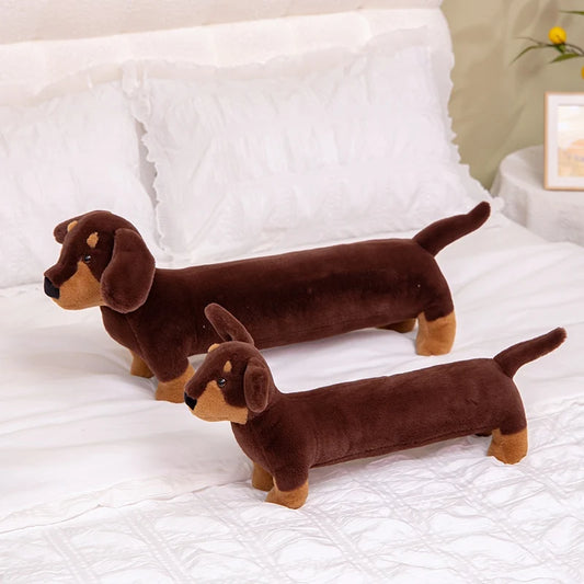 Oscar et Plume coussin teckel en peluche long marron foncé en duo posé sur lit blanc