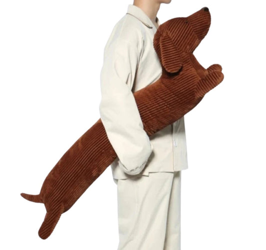 Grand oreiller chien teckel en tissu côtelé marron tenu par une personne en pyjama blanc