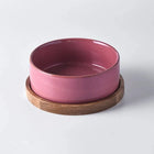 Gamelle en céramique rose sur support en bois pour chien, design élégant et fonctionnel.