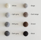 Palette de couleurs naturelles pour cocon en laine tyrolienne, incluant blanc, gris clair, gris moyen, gris foncé, beige, beige foncé, brun, et noir.