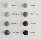 Palette de couleurs naturelles pour cocon en laine tyrolienne, incluant blanc, gris clair, gris moyen, gris foncé, beige, beige foncé, brun, et noir.