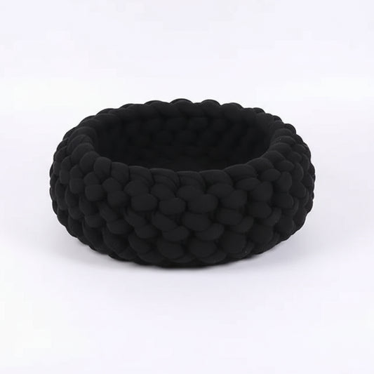 Panier design pour chat noir tricoté à la main, cosy et moderne, sur sol en bois avec décoration