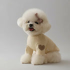 Petit chien blanc portant un pull pour petit chien beige avec un motif cœur marron